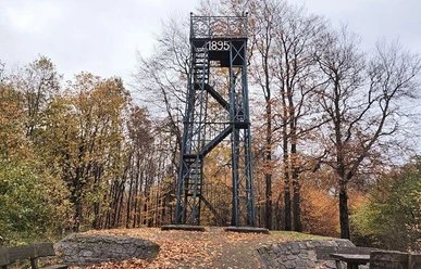 Ein Aussichtsturm aus dem Jahr 1895 steht in einem herbstlichen Wald. Die Umgebung ist mit buntem Laub geschmückt.