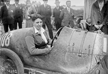 Violette Morris 1927 am Steuer eines Rennwagens, umringt von Zuschauenden