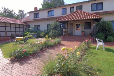 "Sonnenschein" Pension Haus Stork Ein zweigeschossiges Haus mit rotem Dach und Terrasse, umgeben von Rasenflächen und blühenden Beeten.