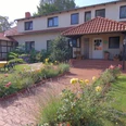 "Sonnenschein" Pension Haus Stork Ein zweigeschossiges Haus mit rotem Dach und Terrasse, umgeben von Rasenflächen und blühenden Beeten.