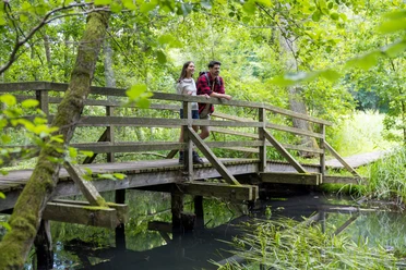 Ein Paar steht im Wald auf einer Brücke im Hellbachtal.