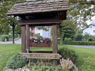 Hölzerne Ortseingangstafel von Tietelsen, bepflanzt mit Blumen, auf einer Rasenfläche