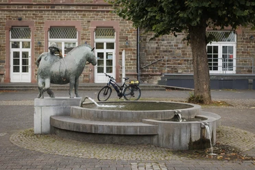 Brunnen mit Bronzeskulptur „Junge mit Grubenpferd“ vor historischem Gebäude in Overath