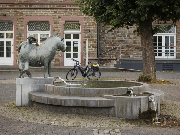 Brunnen mit Bronzeskulptur „Junge mit Grubenpferd“ vor historischem Gebäude in Overath