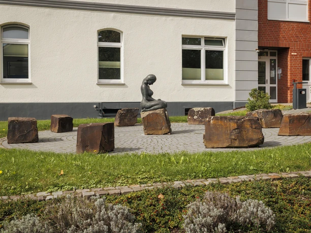 Bronzefigur „Bewahrende“ auf Steinen vor einem Gebäude in Overath