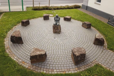 Skulptur „Bewahrende“ auf rundem Pflasterplatz mit Steinen in Overath