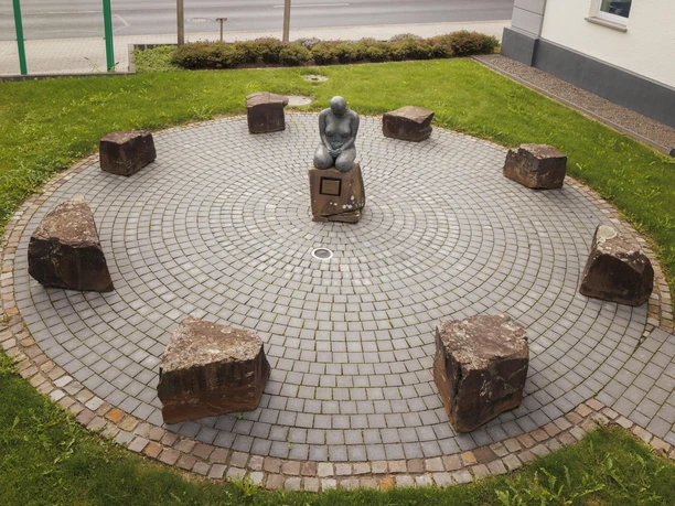 Skulptur „Bewahrende“ auf rundem Pflasterplatz mit Steinen in Overath