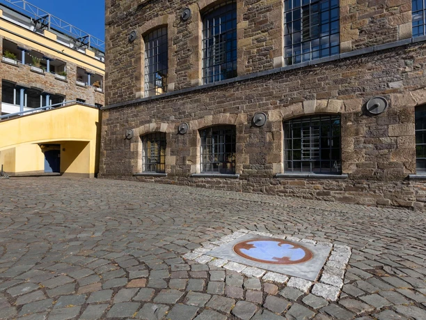 Bodenplatte Engel der Kulturen auf gepflastertem Platz vor historischem Steingebäude