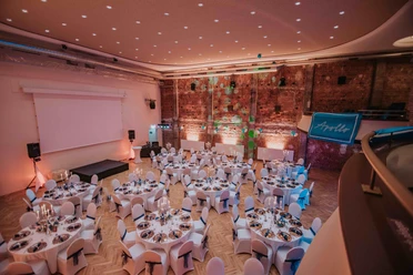 Festlich eingedeckter Apollo-Saal mit Rundtischen, Bühne und beleuchteter Backsteinwand.