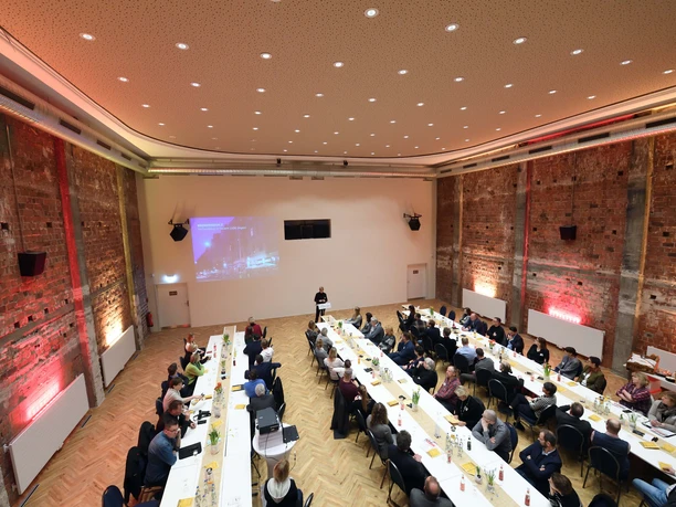 Tagung im Apollo Bremerhaven mit langen Tischreihen, Backsteinwänden und Präsentation.