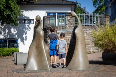 Zwei Kinder betrachten die Bronzeskulptur „Kommunikation“ auf einem Platz in Bielstein