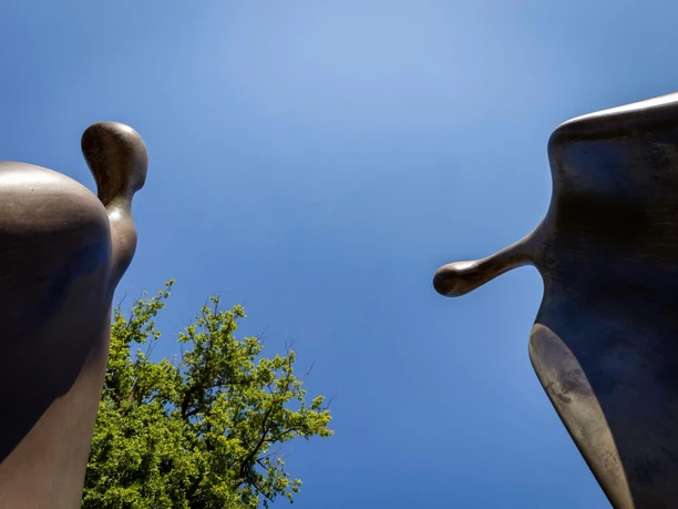 Bronzeskulptur „Kommunikation“ mit zwei abstrakten Figuren vor blauem Himmel.