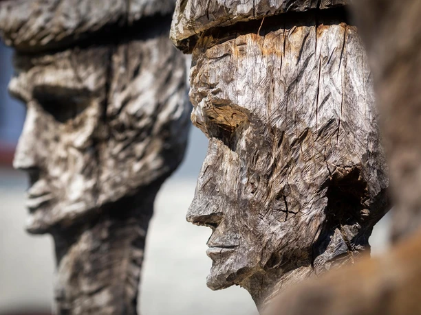 Nahaufnahme der Holzskulptur „Könige“ mit zwei geschnitzten Gesichtern im Profil
