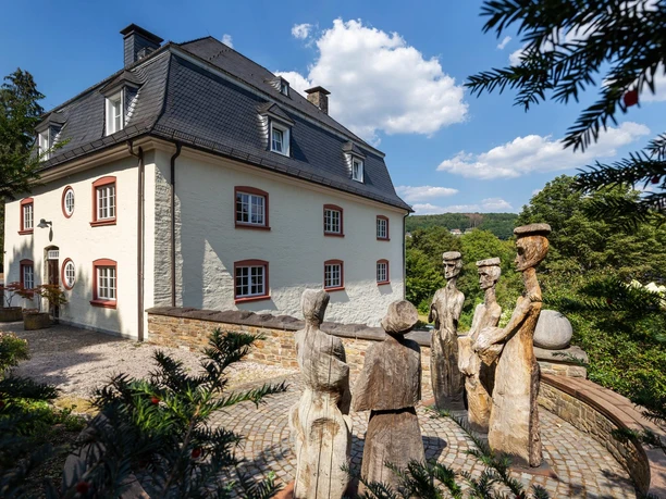Holzskulptur „Könige“ vor hellem Haus mit Schieferdach in Wiehl-Bielstein