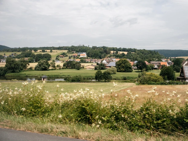 PS.SPEICHER Rallye 2026 Blick über blühende Wiesen auf ein Dorf an einem Flusslauf in hügeliger Landschaft bei Einbeck.