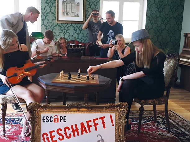 Skupina v únikové místnosti Escape Leipzig řeší úkoly s šachovnicí, houslemi a kamerami.