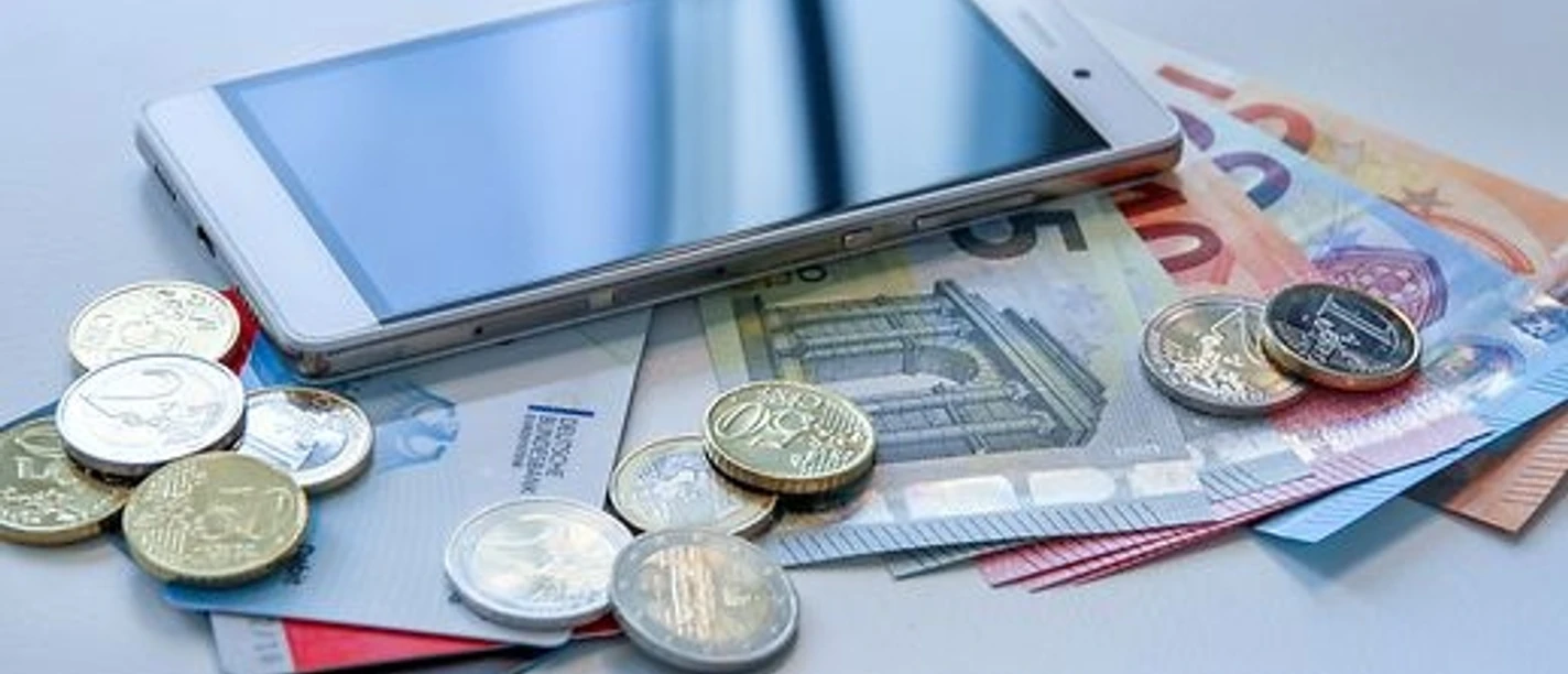 Smartphone liegt auf Euro-Banknoten und -Münzen.
