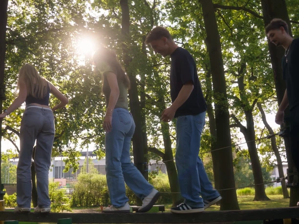 Balance.jpg Vier junge Menschen balancieren auf einem Balken.