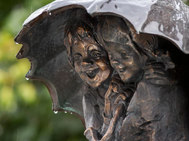 Kinder unterm Regenschirm Bronzeskulptur zweier Kinder unter nassem Regenschirm im Regen