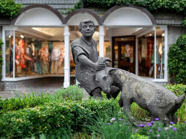 Skulptur Ziegenbrunnen mit einem Jungen und einer Ziege vor Schaufenstern in Waldbröl