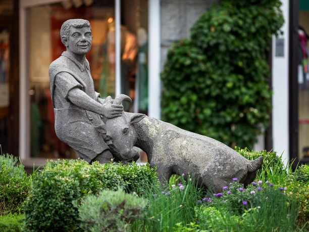 Steinfigur eines Jungen mit Ziege am Ziegenbrunnen in Waldbröl, umgeben von Grün