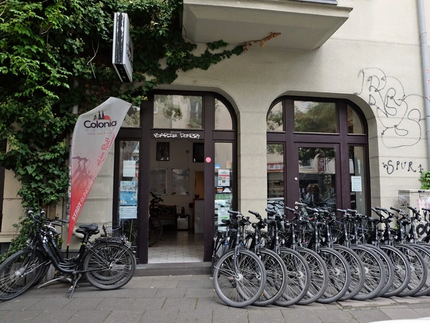 Fahrräder vor dem Eingang von Colonia Aktiv in Köln mit Fahne und begrüntem Fassadenrand