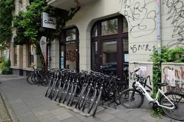 Fahrräder vor dem Colonia-Aktiv-Laden an einer begrünten Kölner Häuserfassade