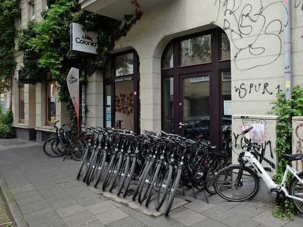 Fahrräder vor dem Colonia-Aktiv-Laden an einer begrünten Kölner Häuserfassade