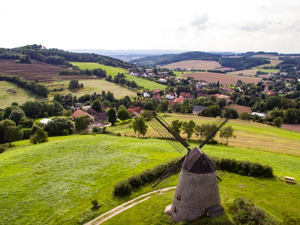 Historische Windmühle umgeben von sanften Hügeln und Feldern, mit Ausblick über das ländliche Gebiet.