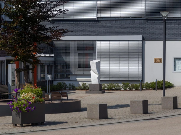 Weiße Steinskulptur „Kraft II“ auf einem Platz vor moderner Fassade in Nümbrecht