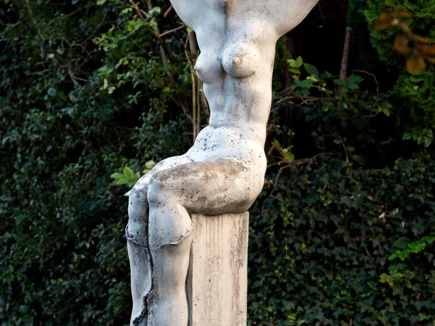 Weiße Figurenskulptur „Erinnerung an einen Baum“ auf Sockel vor dichtem Grün