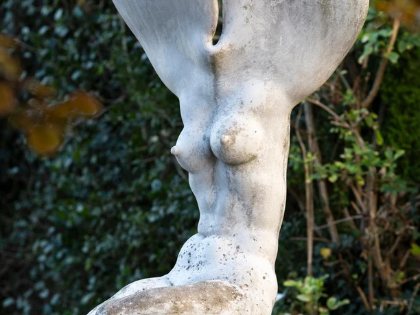 Weiße Skulptur „Erinnerung an einen Baum“ mit weiblicher Form vor grünem Gebüsch