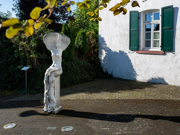 Skulptur „Erinnerung an einen Baum“ vor weißem Haus mit grünen Fensterläden