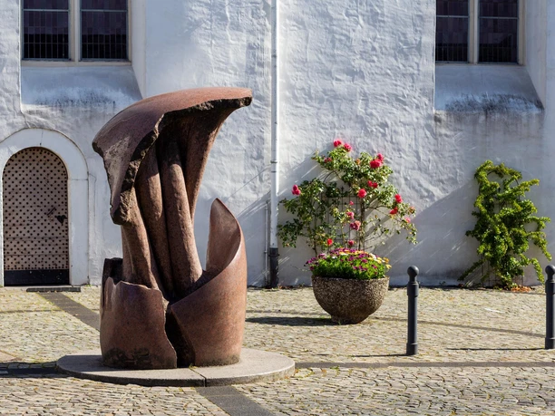 Rostbraune Skulptur „Vergänglichkeit“ von Georg Weber vor weißer Fassade