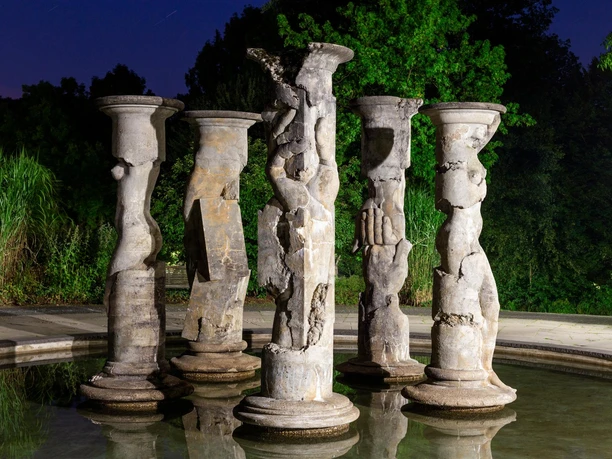 Beleuchteter Säulenbrunnen von Michael Schwarze in Nümbrecht vor dunklem Grün