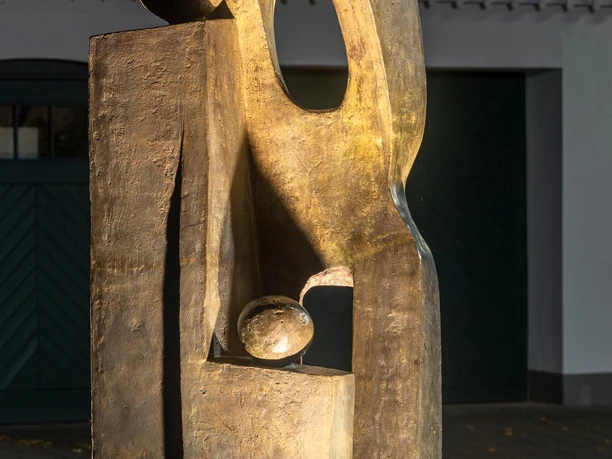 Goldbraune Skulptur „Ein Traum“ mit abstrakten Figuren, nachts angestrahlt