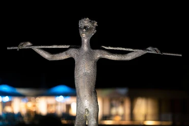 Bronzeskulptur „Knabe mit Stab“ in Nümbrecht vor nächtlich beleuchtetem Hintergrund