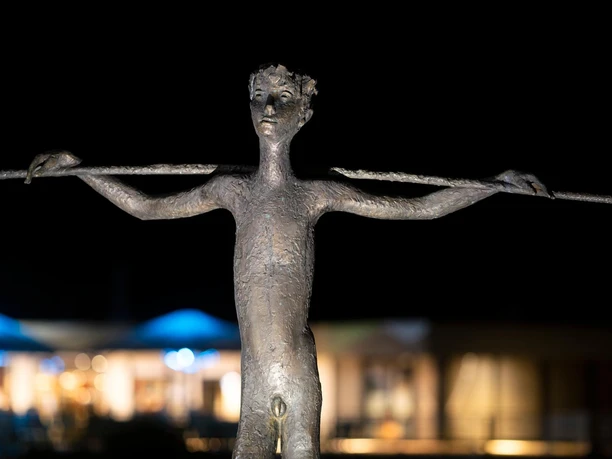 Bronzeskulptur „Knabe mit Stab“ in Nümbrecht vor nächtlich beleuchtetem Hintergrund