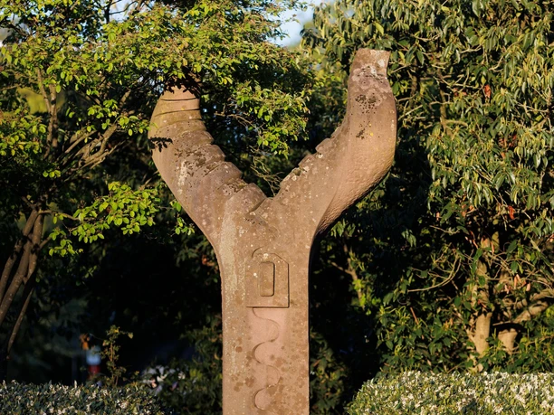 Steinskulptur „Freundschaft“ zwischen grünen Sträuchern im Sonnenlicht
