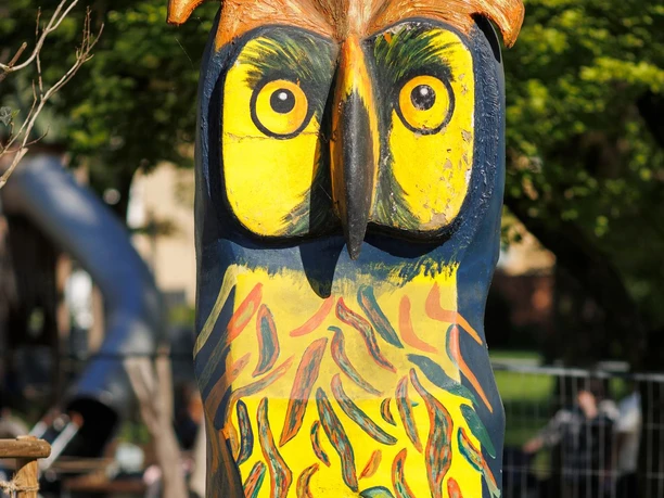 Bunte Eulenskulptur mit gelben Augen und bemaltem Gefieder im Stadtpark.