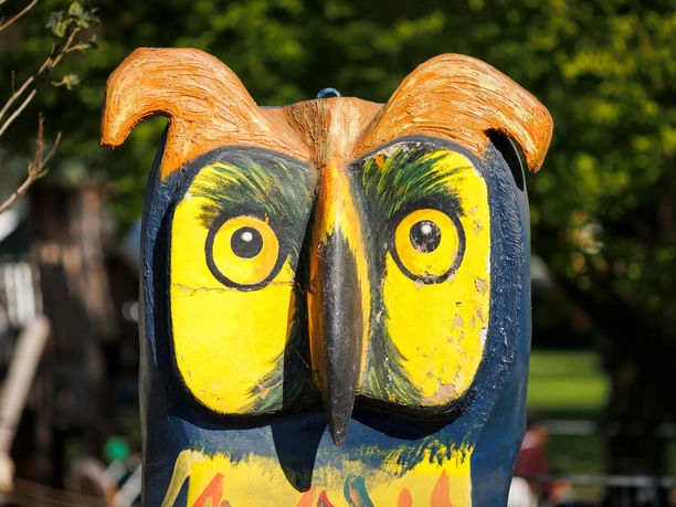 Bunte Eulenskulptur von Mike Kinne mit gelben Augen im Grünen
