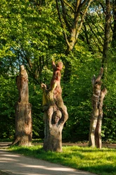 Drei Holzskulpturen mit menschlichen Figuren im grünen Sinneswald bei Sonnenlicht