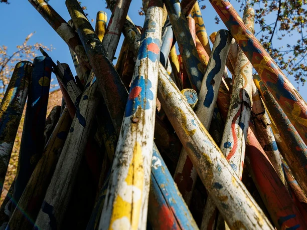 Bemalte Buntstifte-Skulptur von unten, dahinter blühende Äste vor blauem Himmel