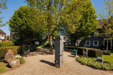 Friedrich-Ueberweg-Platz Steinernes Denkmal auf dem Friedrich-Ueberweg-Platz, umgeben von Bänken und grünen Bäumen