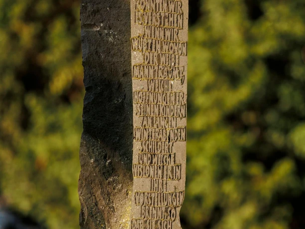 Basalt-Lava-Säule von Berthold Welter mit eingemeißelter Schrift vor grünem Hintergrund