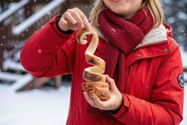 Warmer Baumstriezel Person in roter Jacke hält einen spiralförmigen, frisch gebackenen Striezel in der Hand, während es schneit.