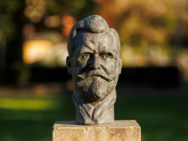 Bronzebüste von Julius Pohlig auf Steinsockel vor unscharfem Parkhintergrund