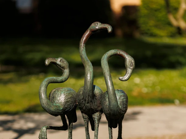 Drei bronzene Flamingo-Skulpturen auf einem Steinsockel im grünen Park