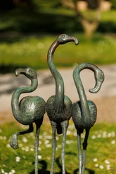 Drei bronzene Flamingo-Skulpturen auf einer Wiese mit unscharfem Parkhintergrund
