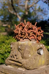 Skulptur „Musik im Kopf“ mit Steinkopf, rotem Röhrenhaar und Hörtrichter im Grünen